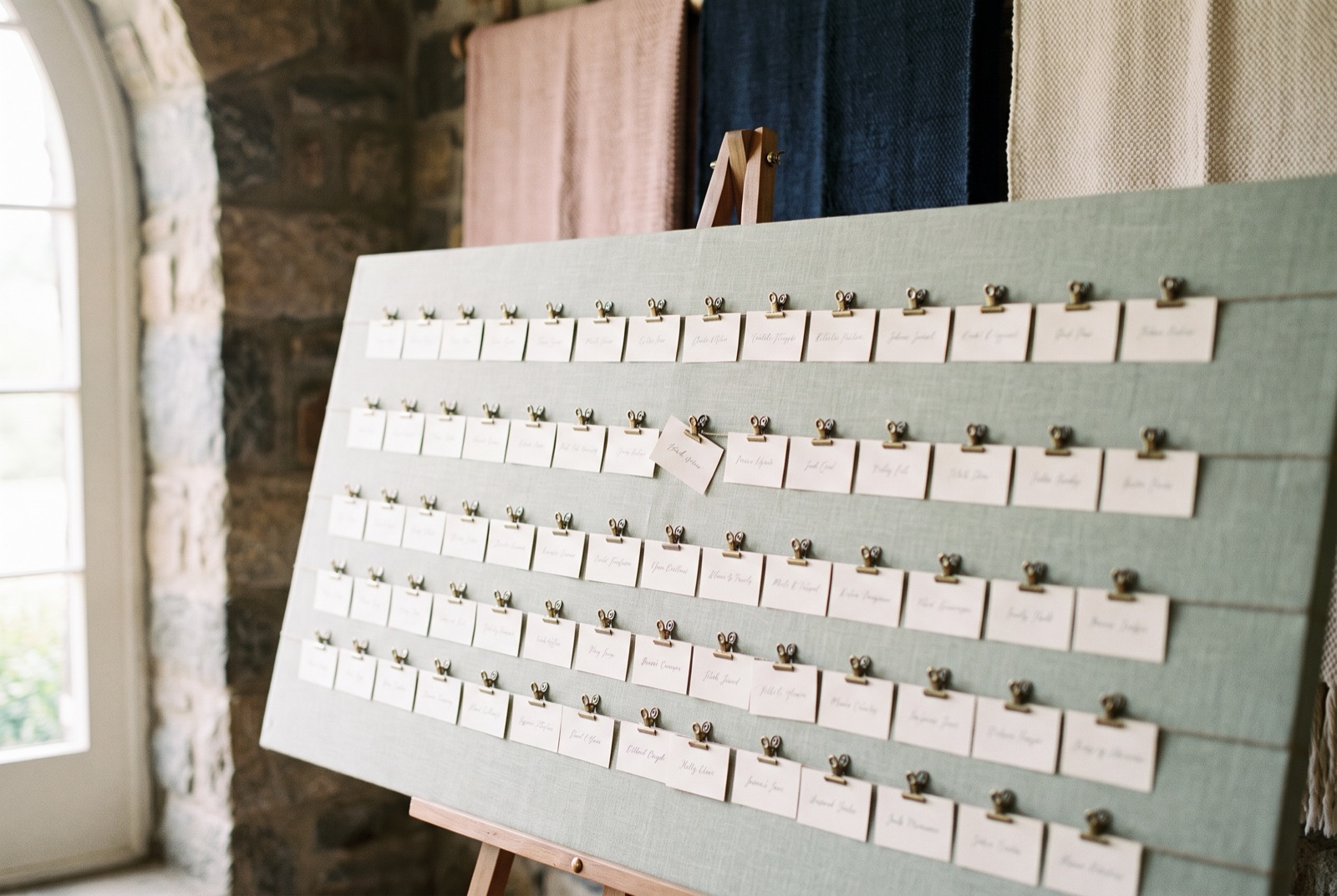 Illustrative wedding place cards on a sage linen board beside a sunlit window